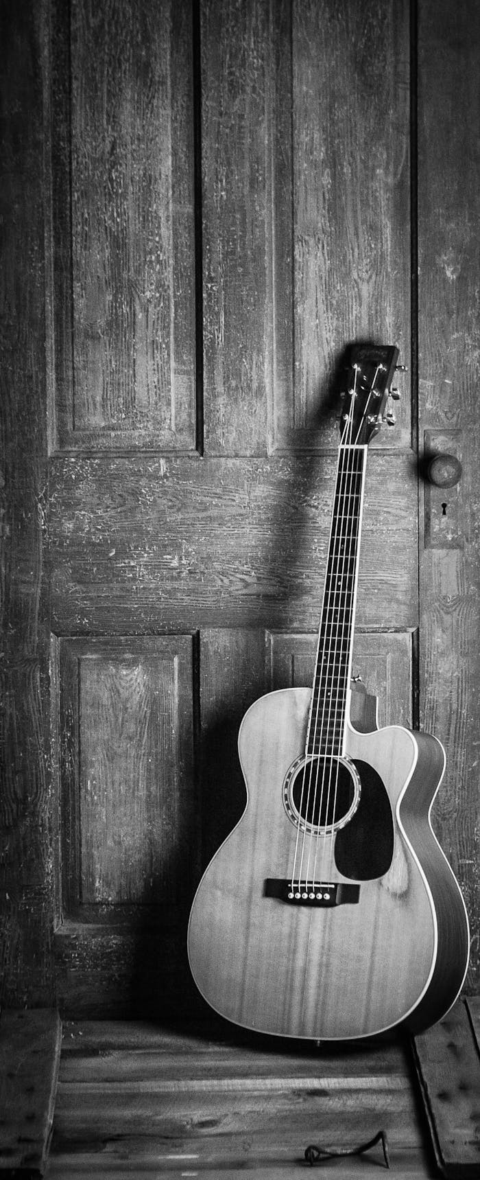 services-01 A classic acoustic guitar leaning against a rustic wooden door in a black and white vintage style.
